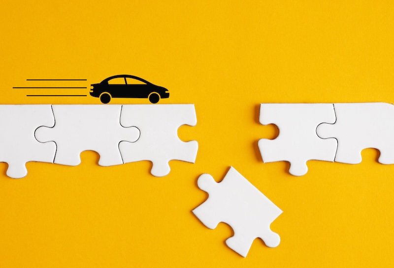 Black car silhouette running over white incomplete puzzle bridge on yellow background. Road risk, danger hazard, accidents and disasters or and car insurance concepts.