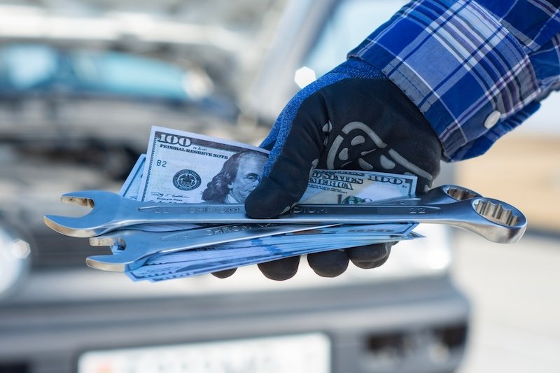 Close up of mechanic hand holding wrenches and dollar cash near car, representing vehicle repair cost and service pricing. Automotive maintenance, financial expense and auto service business concept SSUCv3H4sIAAAAAAAACpySwW6DMAyG75P2DijnIpVBS9mrVDuYxEDUNEFJ6DRVffc5CaDsOokD/mz/9o95vr8VBevBSc4+i2eIKJZKLc5b8NJowsfDyi1qgTYnD1ufjzkAmUcopDdWgsphD55PGu5IUC9KBfyKSeY8+MWhC7usiIPHkTQS3CXSwtcUF1siJqmDUowdMuaWPrINJfF/daaXr93wiJr/xIUzIxYVQjJyTaXs9u3R3nNrsAhpMlcPw0GFgjpTAjmDhT99s5Vc6jEjxk/xLpsSN4v2Nmy1m2HKmBl6Fb76QGNw4xM4R+Vi49lsTn+BuWdztPHR06rKBB0nhFXdVJemqk8dPZema45rQTroJEknrrMJUcxvUuSuZNiAwZmLE2+r8qPDtmyGaiiBi65sh7bqzwjY1he6xesXAAD//wMAjBjGUbkCAAA=