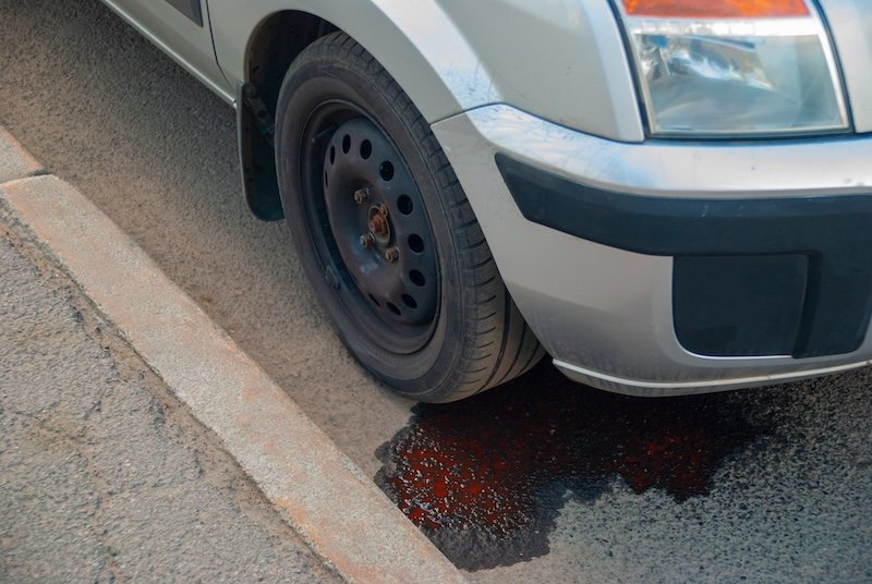 Broken car on the roadside. Oil leak from the engine on the asphalt