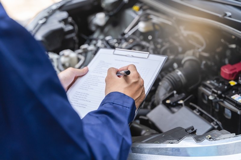Auto check up and car service shop concept. Mechanic writing job checklist to clipboard to estimate repair quotation to client at workshop garage.