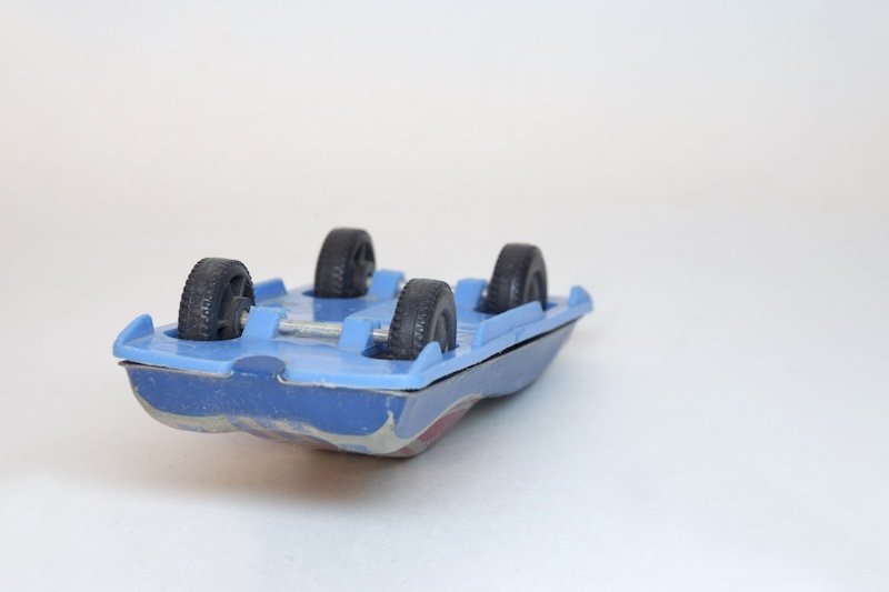 racing car. tin toy. laying on its roof rally toy car, showing plastic blue bottom and black wheels with tire tread pattern, on hidden axle