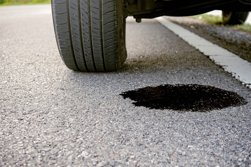 Close up of black engine oil leaks under a broken-down car on the side of the road. Car repair and maintenance concept
